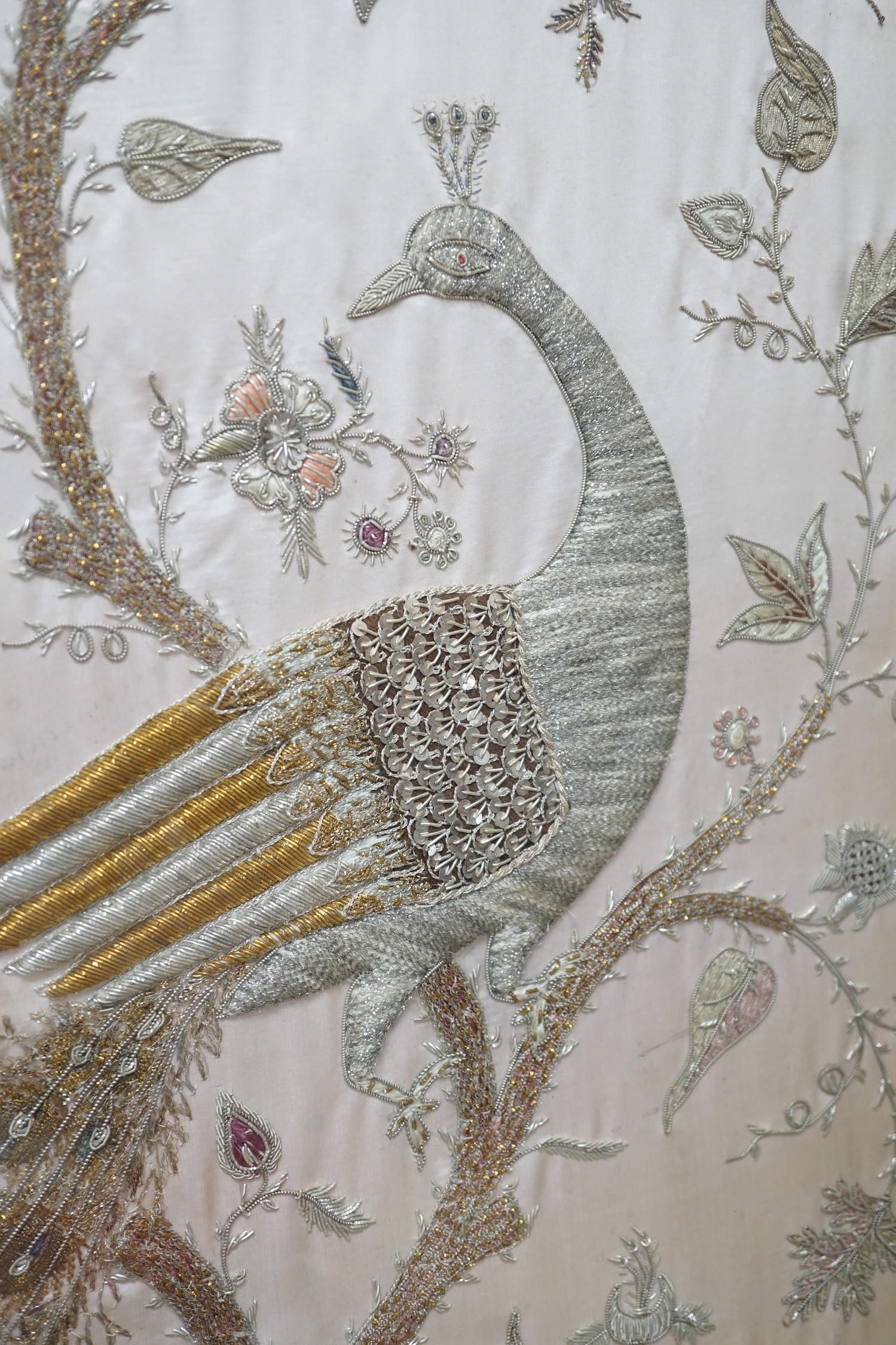 A framed silk, multi coloured metal thread embroidered Indian panel: a peacock seated amongst birds, flowers and leaves in a tree, 110cms x 51cms